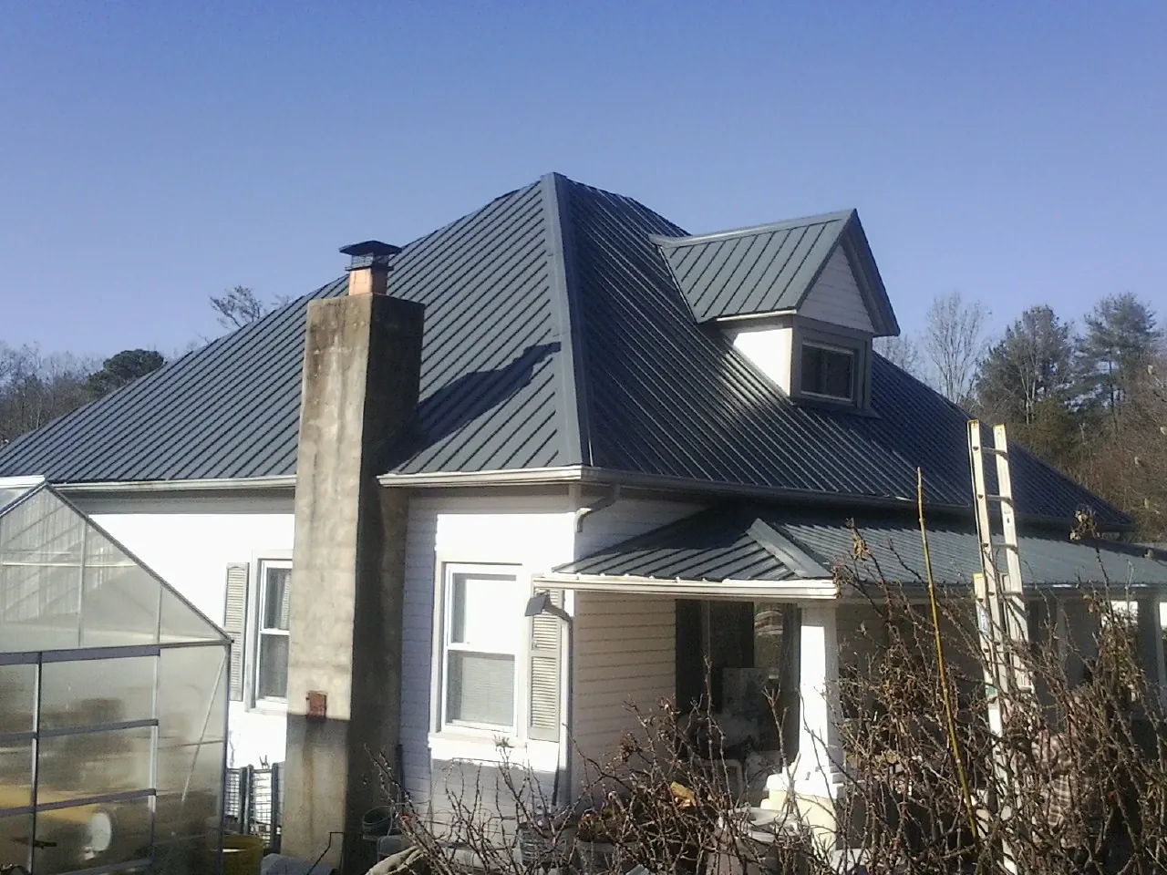 Dark blue standing seam metal roof on a white farmhouse with dormer — Slate & Tile Roof Repair by Roofing Brothers in Tar Heel
