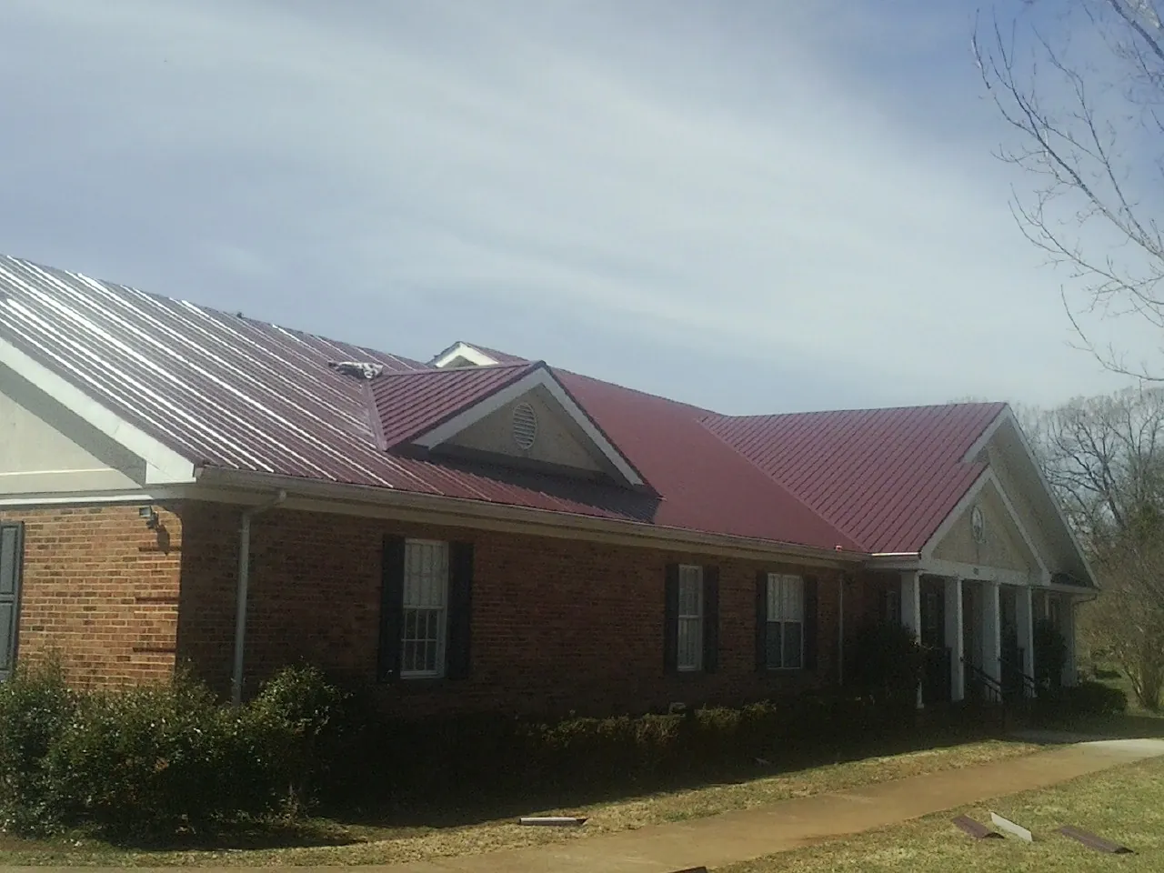 Red metal roof with gabled entries on a long brick building, from a Hail Damage Roof Repair job in Tar Heel