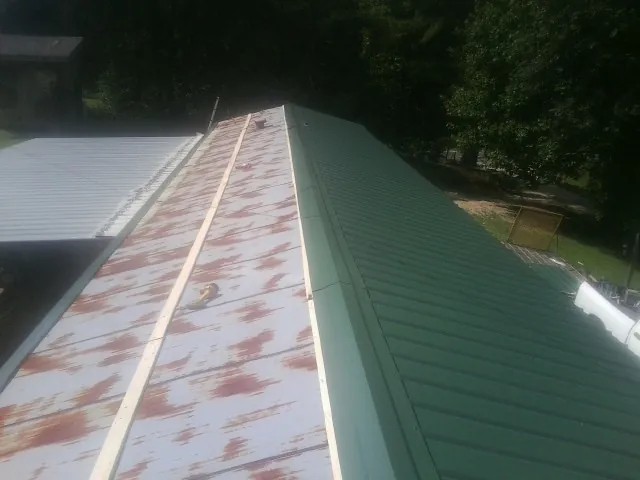 Old rusted panels beside newly installed green metal roofing — Wind Damage Roof Repair by Roofing Brothers in Tar Heel