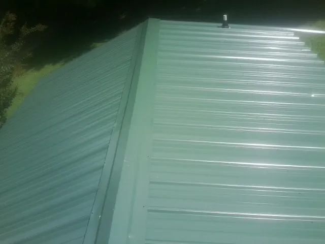 New green metal panels meeting at the ridge of a roof — Flat Roof Repair work by our crew in Tar Heel