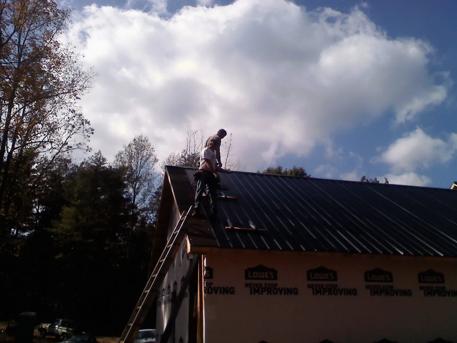 Roofer fastening dark metal panels high against a cloudy sky, from a Roof Inspection job in Tar Heel