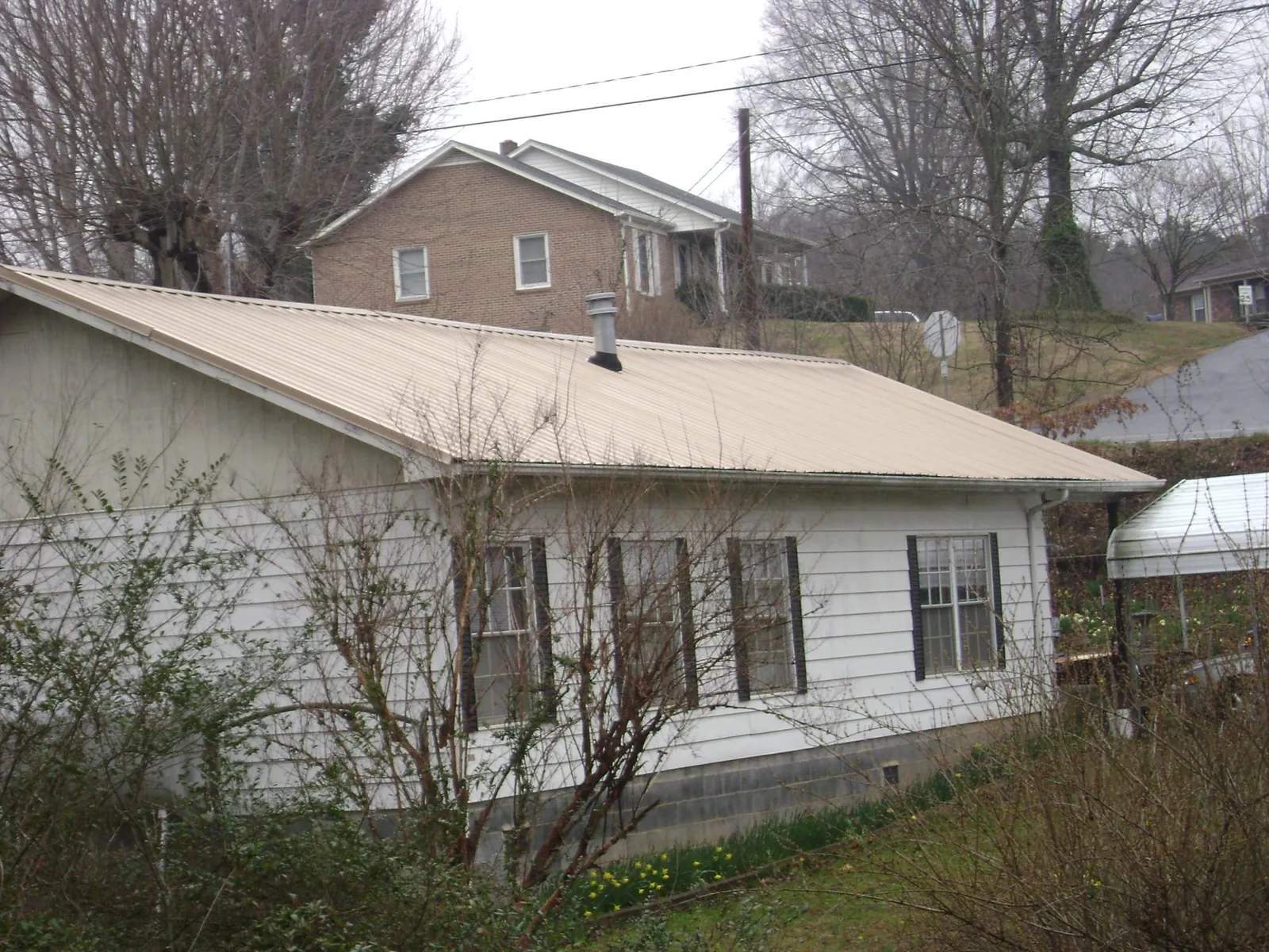 Tan metal roof on a white sided house set into a hillside — Commercial Roofing by Roofing Brothers in Tar Heel
