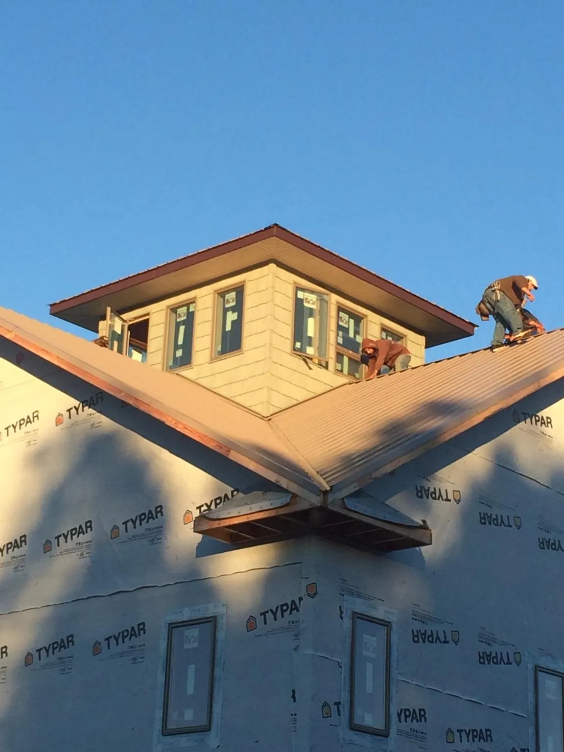 Roofers working around a rooftop cupola on a new metal roof at sunset — Roof Waterproofing in Tar Heel by Roofing Brothers